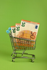 Euro banknotes in shopping cart over green