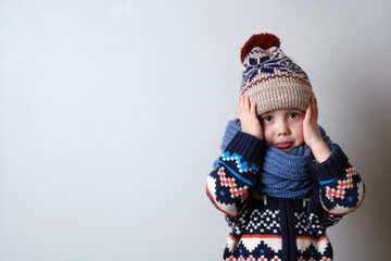 Sick child in clothes, toddler boy is standing on the grey background with a fever. llness child. Boy touches his head