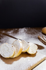 Sliced French baguette on a wooden board, cinnamon sticks and a large spoonful, heavily floured on a wooden table with a black background in the back. Top view with place for text or logo.