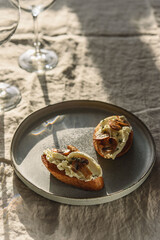 Bruschettas or toasts with cheese and fried mushrooms with thyme served with glasses of wine on greige linen tablecloth