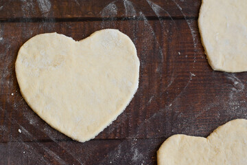 Bakery items - uncooked yeast dough in heart shape on wooden flour background