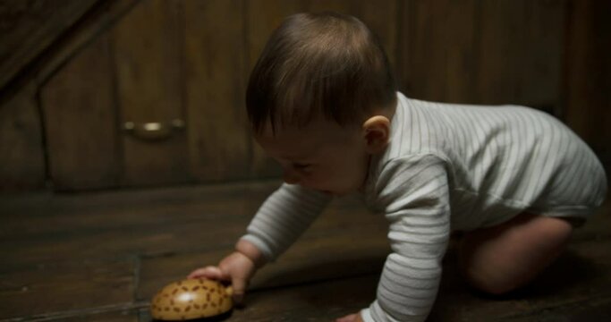 A little baby at home on the floorboards picks up a wooden toy to chew on it