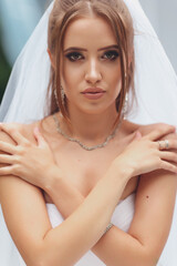 Fototapeta premium Beautiful bride in a magnificent wedding dress posing among greenery on the street. Bride concept for advertising dresses