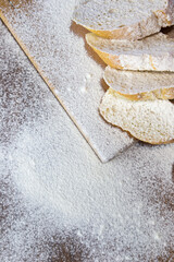 Sliced French baguette on a wooden board, heavily floured on a wooden table. Top view with place for text or logo.
