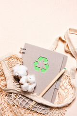 Mesh bags and reusable notepad with green recycling sign on a beige background. Zero waste and sustainable lifestyle concept.