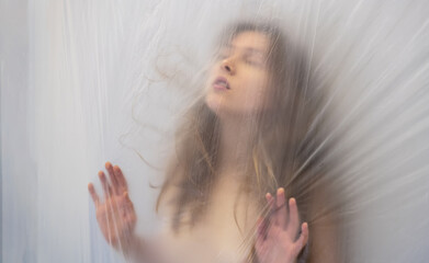 Blurred, out of focus portrait of beautiful sexy sensual woman behind transparent plastic foil in a...