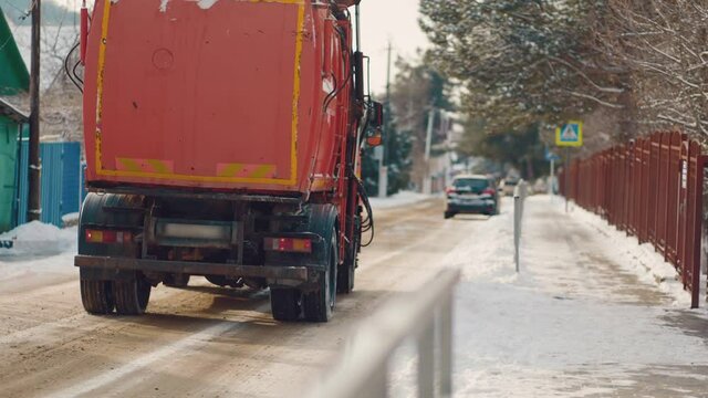 A truck with sand is driving on a snow-covered street. Rear view. Slow motion. Cleaning services.