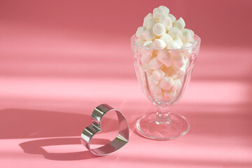 Sweet marshmallows in the glass with a heart and pink background. Holiday food concept.