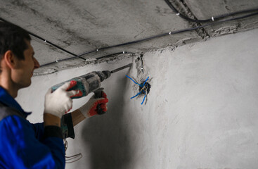 Electrician man drills holes in a concrete wall. Professional drill for making holes in walls. Rear view with diamond drill and operator installed