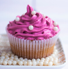 muffin with lilac color cream decorated with edible pearls on a saucer stands on a wooden background. Festive cake with cream. cream cheese, butter cream. Fresh bakery. Birthday dessert. small cake. 