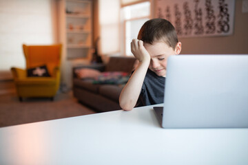 boy covering his eyes while looking at a laptop