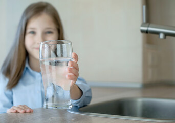 Happy little girl holding a glass of water. Selective focus on child hand with glass of water in...