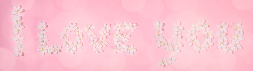 Wide festive banner. Inscription I LOVE YOU laid out from flowers of white apple tree on pink backdrop with bokeh. Holiday Mother's day, Valentine's Day, Wedding floral concept. Top view, flat lay.