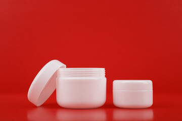 Two white glossy cream jars against red background with copy space. Concept of luxury skin care or daily beauty treatment