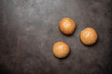 Fresh homemade sesame buns for a hamburger on a dark rustic background. Top view, flat lay, copy space.