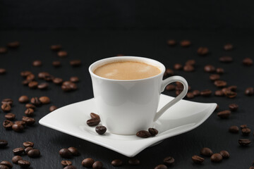 White cup of coffee on a black background. Coffee beans on a black table. Close-up side view, macro photography.