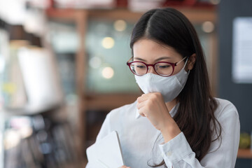 COVID-19 outbreak has caused asian businesswoman must wear a mask to work at the office. Young asia woman suffer from cough with face mask protection.