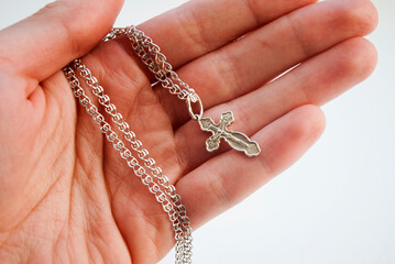 Silver Christian cross in a female hand on a white background.