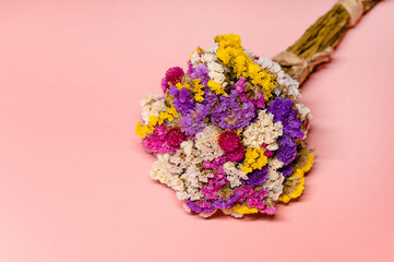 Close up flat lay photo of a beautiful colorful bunch of dried everlasting flowers on a pink background.