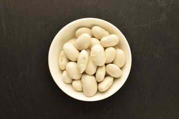 Dried grains of organic white beans in a ceramic dish on a slate board, top view.