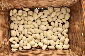 Dried grains of organic white beans in a basket of vines, top view.