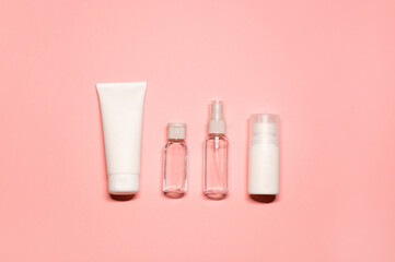 Minimal flat lay shot with beauty products: tube of hand cream, facial mist, toner, and cleansing foam on a pastel pink background.