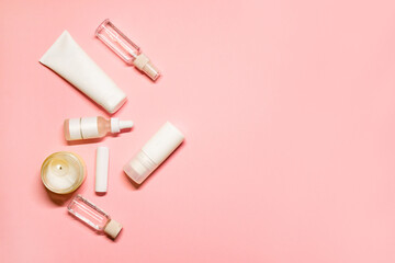 Flat lay shot with a copy space on a pink background with skincare goods: hand cream, deodorant, lipstick, facial serum, essential oil with a lighted candle.
