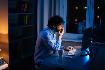 Side view of tired young business man working on computer in home at night. Focused freelancer...