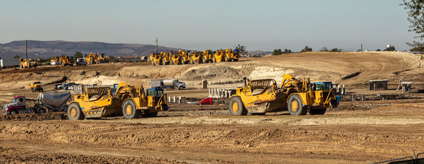 Earth moving equipment at a construction grading site with other tractors lined up in the background - obrazy, fototapety, plakaty