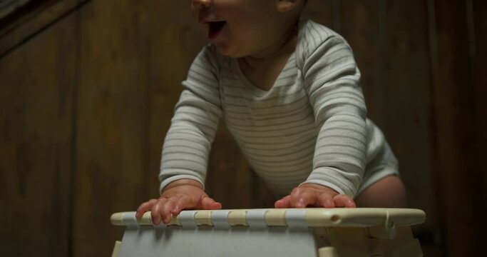 A little baby is standing up by using a foot stool as support