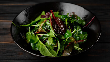 fresh salad with arugula, spinach and olive oil in black plate. healthy food lifestyle