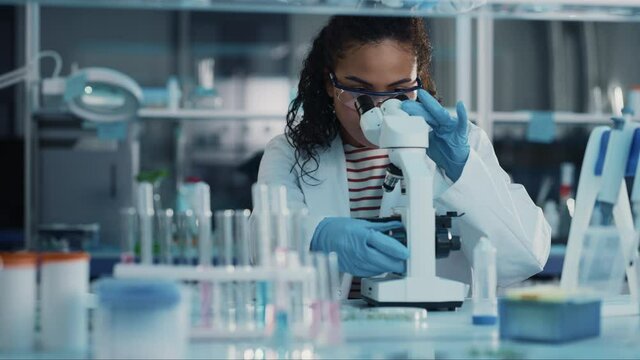 Medical Science Laboratory: Portrait of Beautiful Black Scientist Looking Under Microscope Does Analysis of Test Sample. Ambitious Young Biotechnology Specialist, working with Advanced Equipment