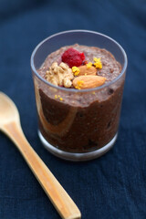 Glass of chocolate, orange and chia seed pudding with nut and raspberry topping. Selective focus, dark blue background.