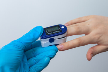 Doctor's hand in blue gloves checks the oxygen saturation of the patient using an oximeter