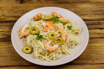 Spaghetti pasta with prawns, green olives and parsley on wooden table