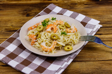 Spaghetti pasta with prawns, green olives and parsley on wooden table