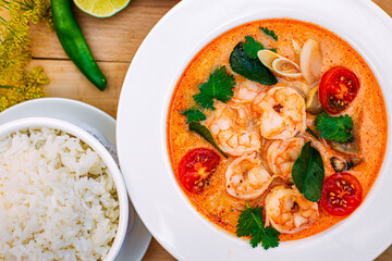 Thai soup tom yam with shrimps and tomatoes and rice as a garnish on a decorated table