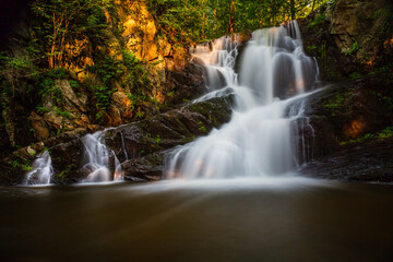 Fototapeta na wymiar Long exposure of small waterfall in summer woods at sunset