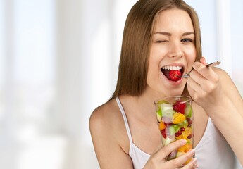 Young woman eating fruits from glass on blurred background