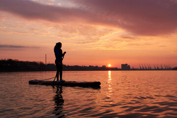 Fototapeta na wymiar Silhouette of a young woman standing on a SUP during a beautiful winter sunrise on the river
