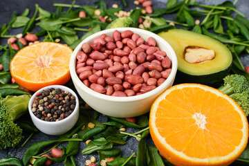 peanut beans in a bowl lie on a stone table next to avocado greens and an orange