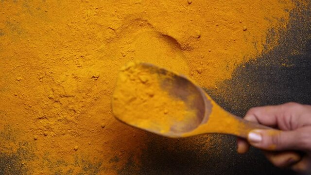Indian spices turmeric powder in wooden spoon falling on black background, Kerala India Sri Lanka traditional Indian curry masala 4K slow motion video footage, antiseptic antiviral Ayurvedic medicine.