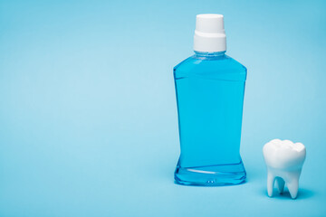 White model of tooth and bottle of mouthwash on blue background with copy space