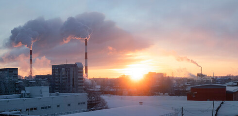 Cogeneration or combined heat and power station in outskirts of town in frosty winter day. Fume from pipes in the sunset sky.