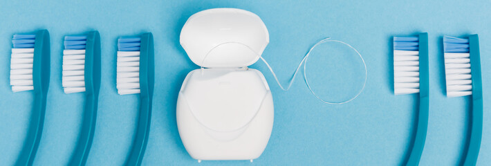 Top view of toothbrushes near dental floss on blue background, banner