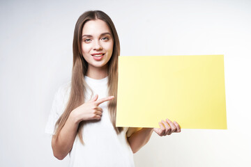 Fototapeta premium A beautiful blonde in a white T-shirt on a gray background holds a yellow sign