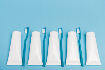 Top view of blue toothbrushes and white tubes of toothpaste on blue background