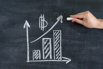 Bitcoin. Cryptocurrency growth graph on a chalk board. Man's hand with white chalk