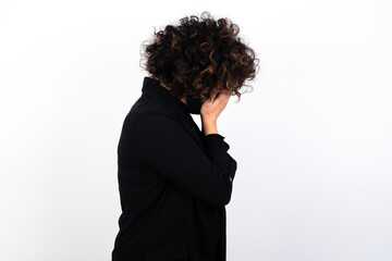 Sad young beautiful caucasian woman wearing medical mask standing against white wall covering face with hands and crying.