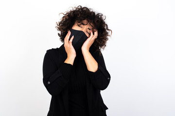 Young gloomy young beautiful caucasian woman wearing medical mask standing against white wall,...